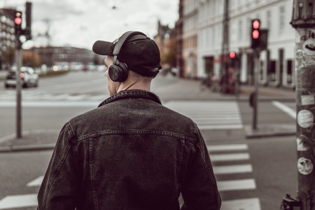 A young man in a cap and headphones waits at a city crosswalk, embracing modern lifestyle.